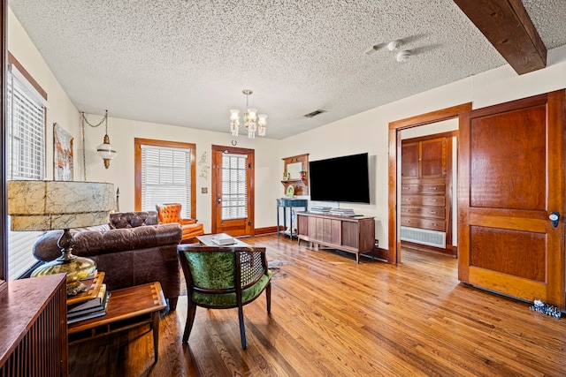 living area featuring visible vents, baseboards, a chandelier, wood finished floors, and a textured ceiling