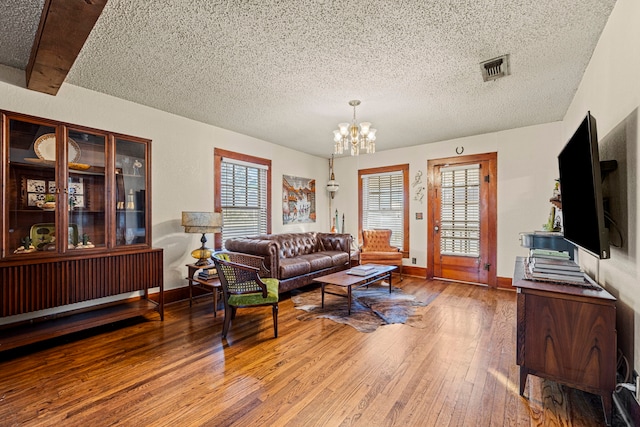 living area featuring visible vents, a notable chandelier, a textured ceiling, hardwood / wood-style floors, and baseboards