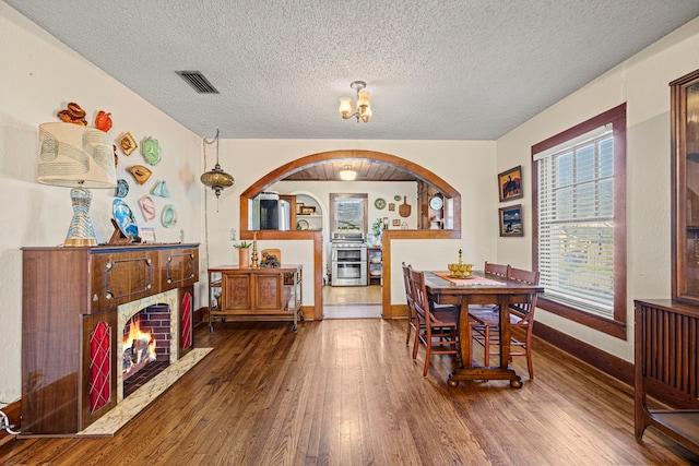 dining space featuring visible vents, baseboards, a lit fireplace, hardwood / wood-style floors, and a textured ceiling