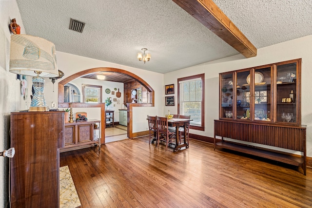 dining space featuring visible vents, beamed ceiling, hardwood / wood-style flooring, arched walkways, and a textured ceiling