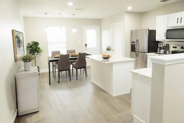 kitchen featuring light wood-style floors, appliances with stainless steel finishes, pendant lighting, white cabinetry, and a center island