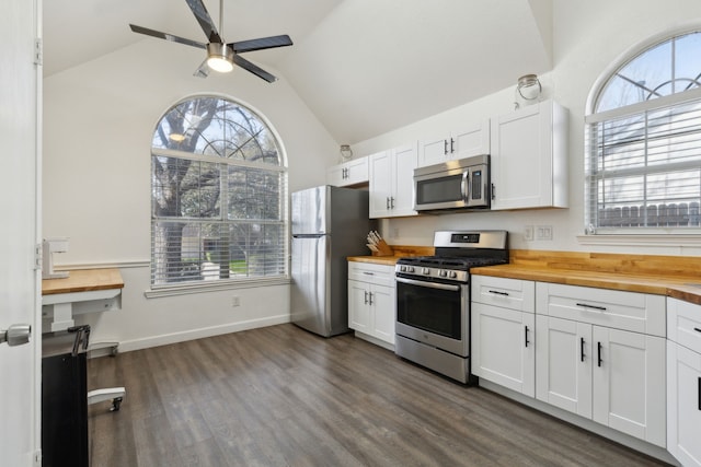 kitchen with dark wood-type flooring, lofted ceiling, stainless steel appliances, white cabinets, and wooden counters