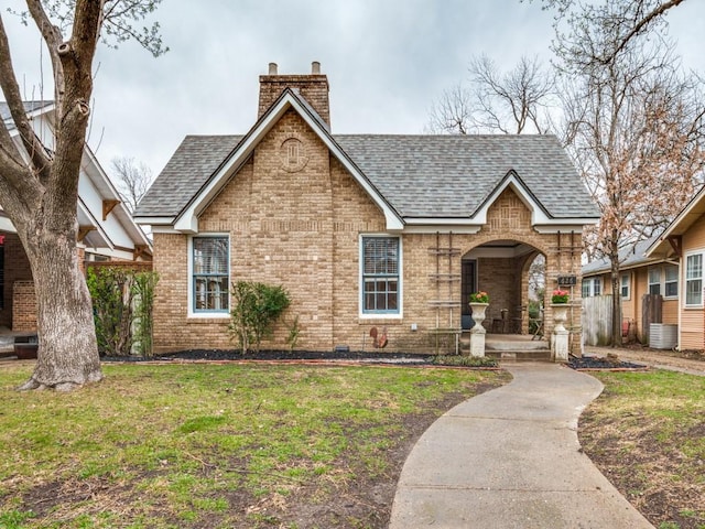 view of front of home featuring central AC unit, roof with shingles, a chimney, a front lawn, and brick siding