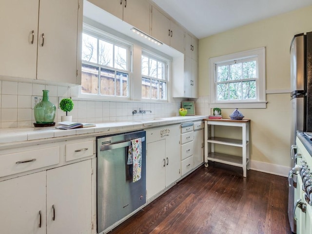 kitchen with dark wood-type flooring, backsplash, stainless steel dishwasher, white cabinetry, and tile counters