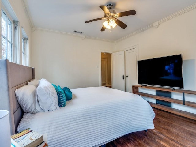 bedroom featuring a ceiling fan, wood finished floors, visible vents, and ornamental molding