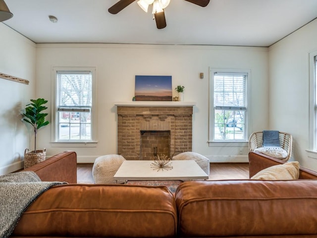 living room with ceiling fan, baseboards, a brick fireplace, and wood finished floors