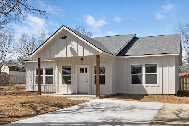 modern farmhouse with board and batten siding, roof with shingles, and fence