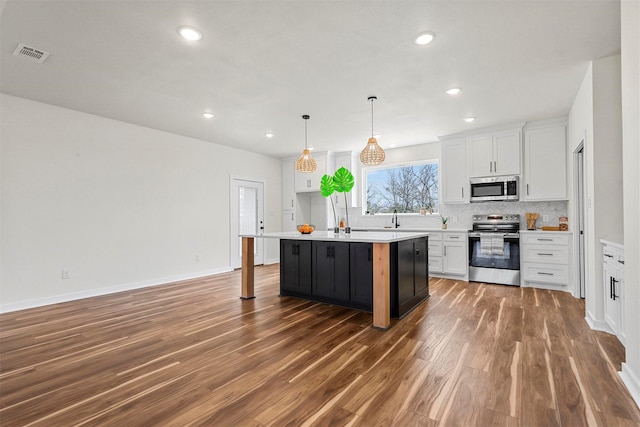 kitchen featuring wood finished floors, visible vents, decorative backsplash, appliances with stainless steel finishes, and white cabinetry