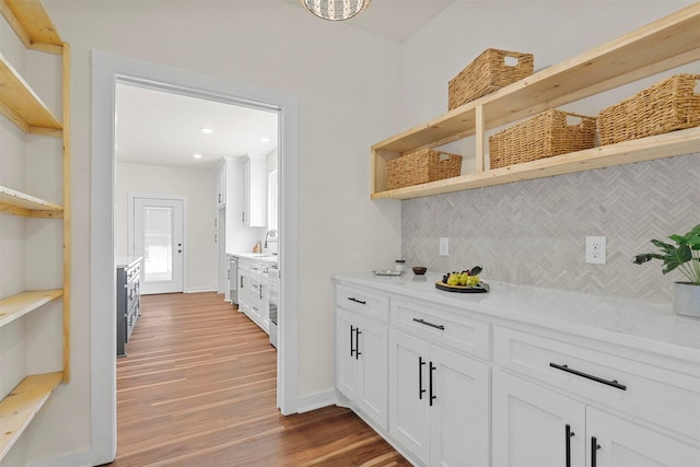 bar featuring baseboards, decorative backsplash, stainless steel dishwasher, wood finished floors, and a sink