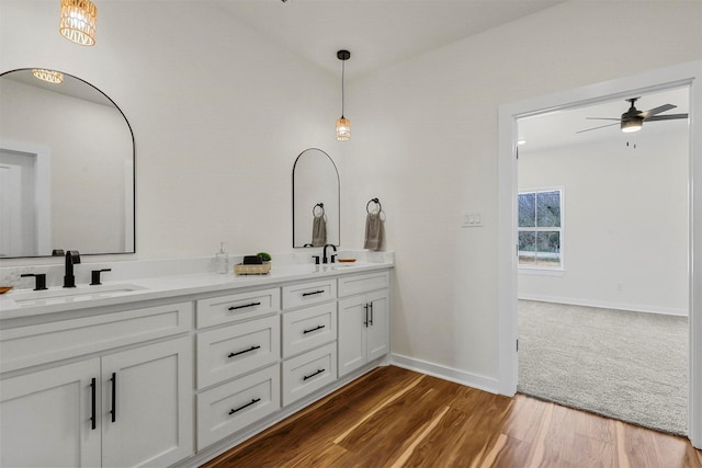 bathroom featuring baseboards, double vanity, wood finished floors, a ceiling fan, and a sink