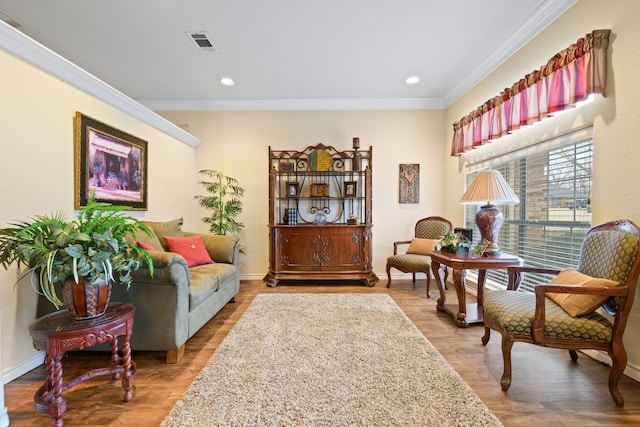 living area featuring baseboards, wood finished floors, visible vents, and ornamental molding