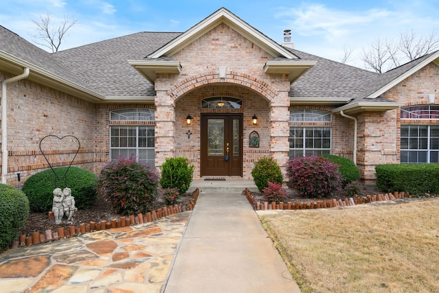 entrance to property featuring a chimney, brick siding, and a shingled roof