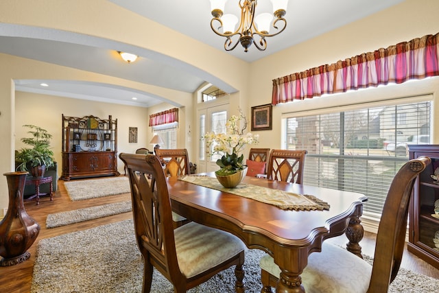 dining area with a chandelier, arched walkways, wood finished floors, and ornamental molding