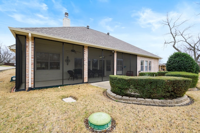 back of house featuring a ceiling fan, roof with shingles, a sunroom, brick siding, and a chimney