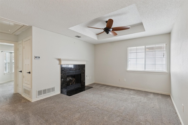 unfurnished living room featuring visible vents, a premium fireplace, attic access, a raised ceiling, and a wealth of natural light