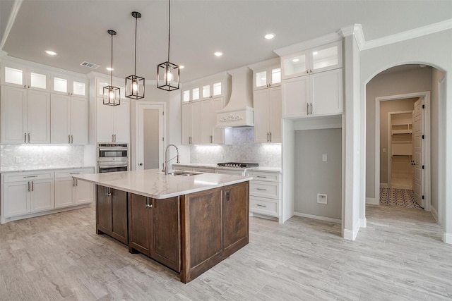 kitchen with visible vents, light countertops, arched walkways, custom exhaust hood, and a sink