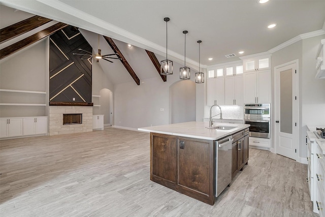 kitchen with arched walkways, a sink, appliances with stainless steel finishes, white cabinetry, and beamed ceiling