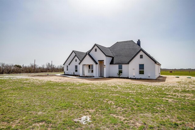 view of front of house with stucco siding, a chimney, a front yard, and roof with shingles