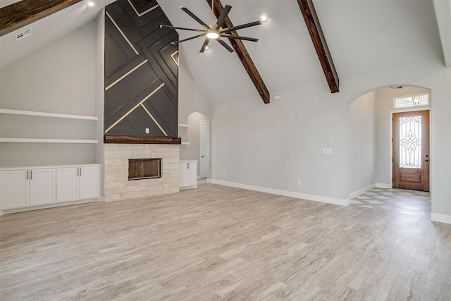 unfurnished living room with arched walkways, a stone fireplace, beam ceiling, and wood finished floors