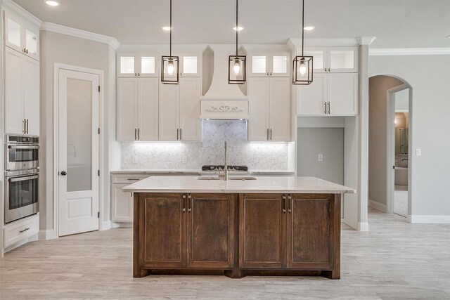 kitchen featuring white cabinetry, crown molding, arched walkways, and stainless steel double oven