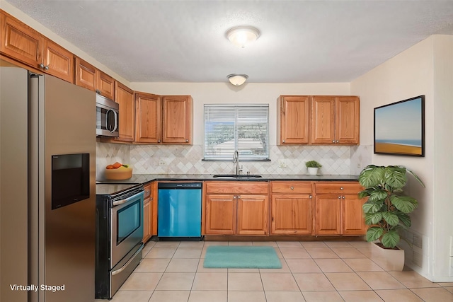 kitchen featuring a sink, tasteful backsplash, dark countertops, brown cabinetry, and appliances with stainless steel finishes