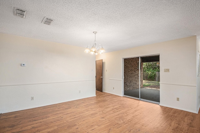 spare room with visible vents, a textured ceiling, an inviting chandelier, and wood finished floors