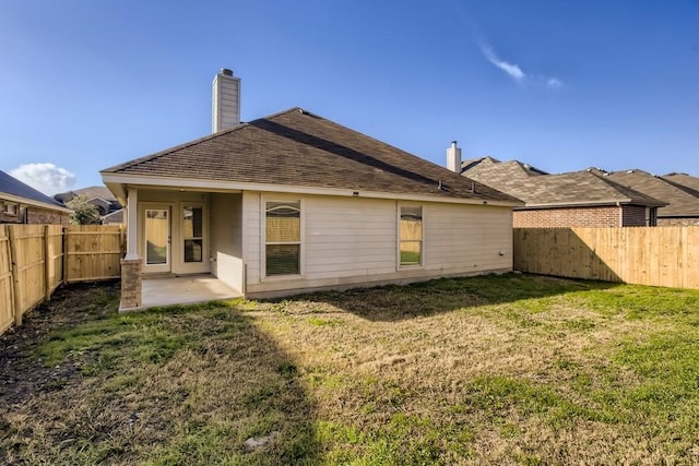 back of property featuring a lawn, a patio, a chimney, and a fenced backyard