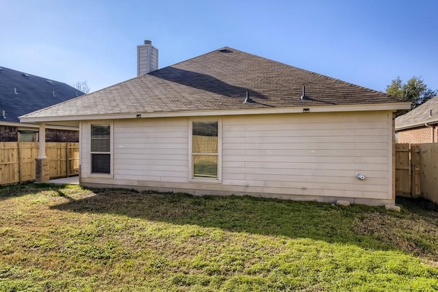 back of house with a shingled roof, a chimney, a yard, and fence