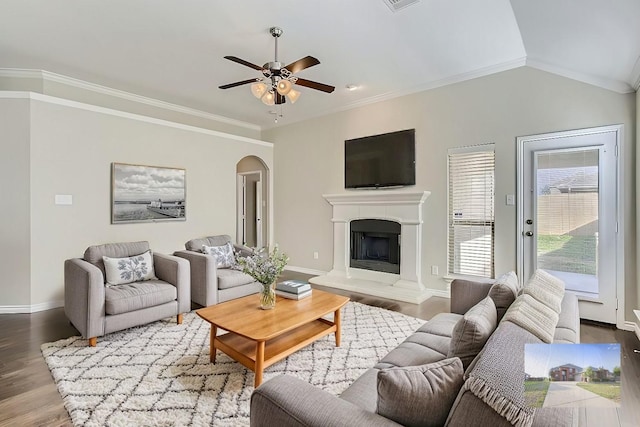 living area with a fireplace with raised hearth, wood finished floors, arched walkways, crown molding, and vaulted ceiling