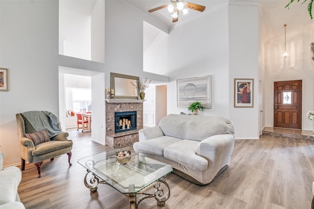 living room with light wood-type flooring, baseboards, ceiling fan, and a tiled fireplace