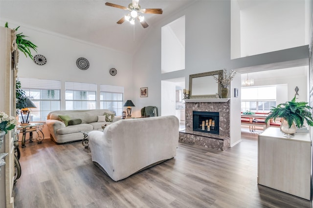 living area with wood finished floors, high vaulted ceiling, a multi sided fireplace, crown molding, and ceiling fan with notable chandelier