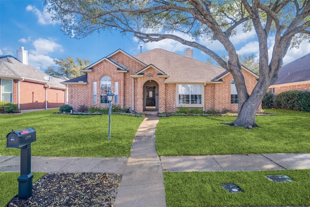 view of front of house with brick siding, a chimney, a front yard, and a shingled roof