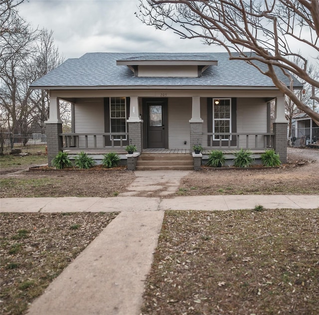 view of front of house featuring brick siding, fence, covered porch, and a shingled roof