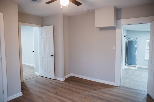 unfurnished room with ceiling fan, baseboards, electric water heater, and wood finished floors