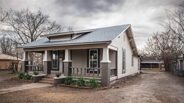 view of front facade featuring fence, covered porch, and roof with shingles