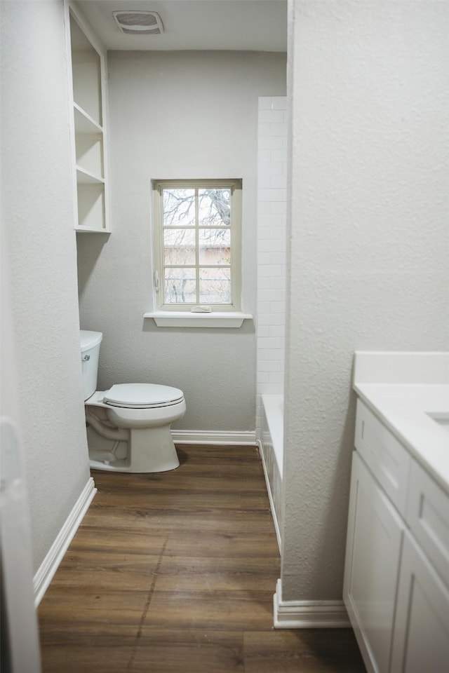 bathroom featuring visible vents, baseboards, toilet, wood finished floors, and vanity