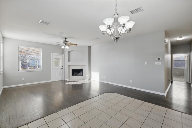 unfurnished living room featuring wood finished floors, a fireplace with flush hearth, ceiling fan with notable chandelier, and visible vents