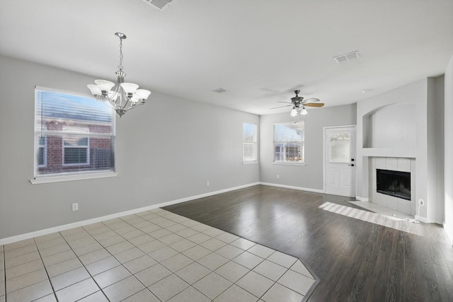 unfurnished living room featuring visible vents, baseboards, ceiling fan with notable chandelier, a fireplace, and wood finished floors