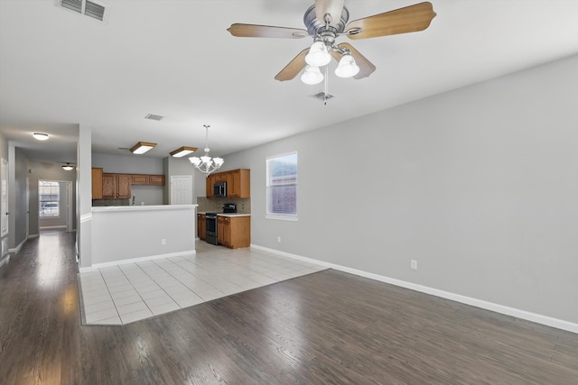 unfurnished living room featuring visible vents, light wood-style flooring, ceiling fan with notable chandelier, and baseboards