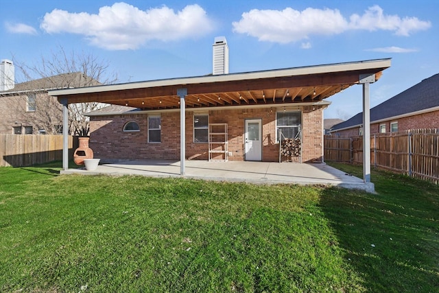 rear view of house featuring a patio, a yard, a fenced backyard, a chimney, and brick siding