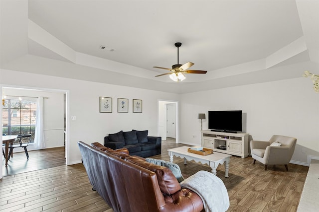 living room with visible vents, baseboards, a tray ceiling, and wood finished floors