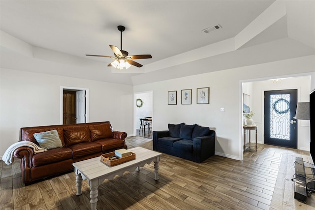 living area featuring a raised ceiling, wood finished floors, visible vents, and baseboards