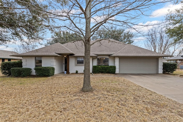 ranch-style home with roof with shingles, concrete driveway, a front lawn, a garage, and brick siding