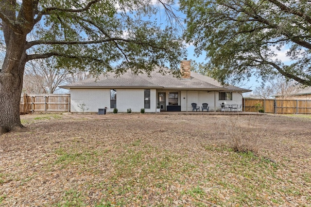 rear view of property featuring a patio area, a fenced backyard, brick siding, and a chimney