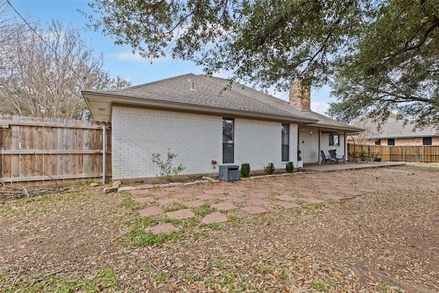 back of property featuring central AC unit, fence, a chimney, a patio area, and brick siding