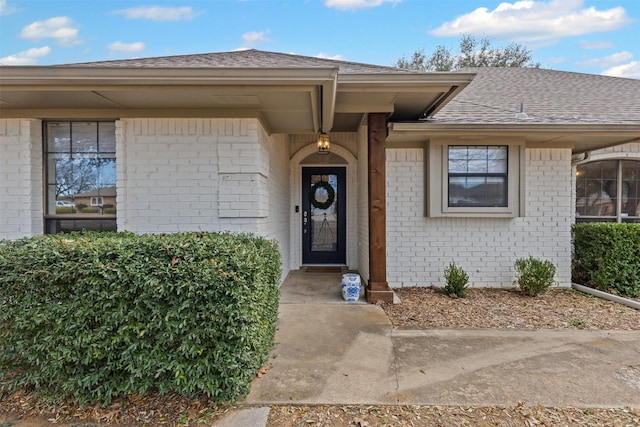 property entrance featuring brick siding and a shingled roof