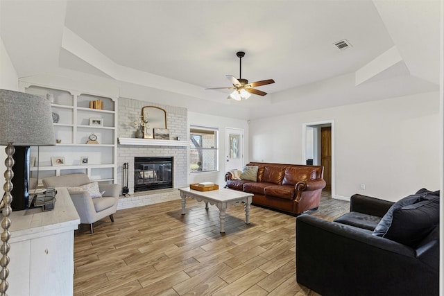 living area with a ceiling fan, visible vents, a tray ceiling, light wood-style flooring, and a fireplace