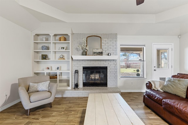 living room with a ceiling fan, a brick fireplace, wood finished floors, and baseboards