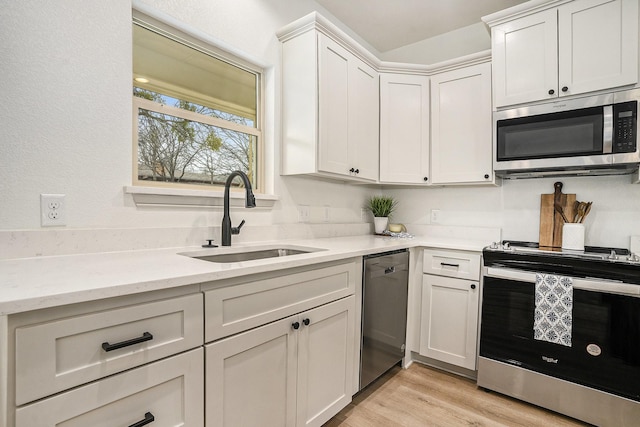 kitchen featuring light wood-type flooring, a sink, light stone counters, white cabinetry, and appliances with stainless steel finishes