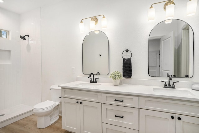 full bathroom featuring a sink, tiled shower, toilet, and wood finished floors